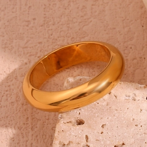 Polished 18K gold-plated stainless steel chunky ring leaning on a beige textured stone