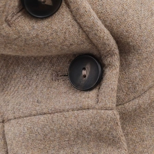 Detailed close-up of light brown wool blend fabric with two black circular buttons