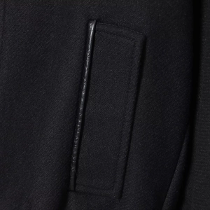 Close-up of black wool jacket featuring a vertical pocket with stylish leather piping detail