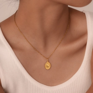 Close-up of a gold oval sunburst pendant necklace worn by a model on a white top