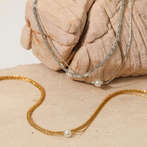 Detail of layered stainless steel anklets with shell pearls on natural stone texture