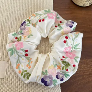 Close-up of floral embroidery on cream satin scrunchie with detailed stitching