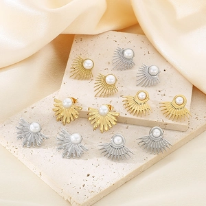 Elegant gold and silver sunburst pearl stud earrings displayed on silk fabric