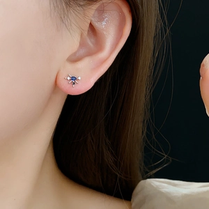 Detail showing a star-shaped silver stud earring with blue gemstone on ear