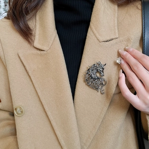 Detail of vintage silver hollow horse brooch pinned on a beige coat for styling