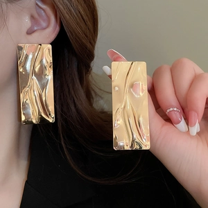 Gold rectangular earrings with liquid lava texture shown on model and held in hand