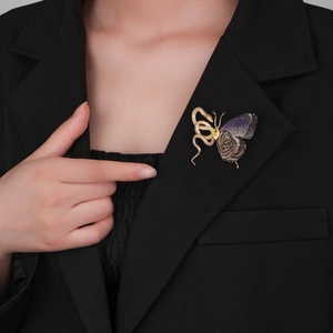Detailed view of an exotic gold snake and butterfly brooch on a black blazer jacket