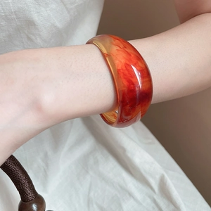 Detail view of wide resin bangle with translucent orange marble texture on wrist