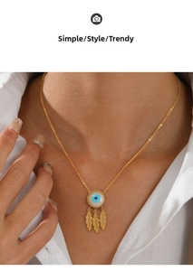 Detail of gold evil eye necklace with leaf pendants worn on neck with white shirt