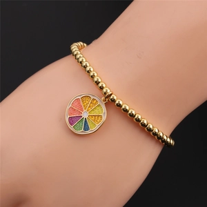 Close-up of a gold-plated beaded bracelet with a colorful rainbow orange slice pendant