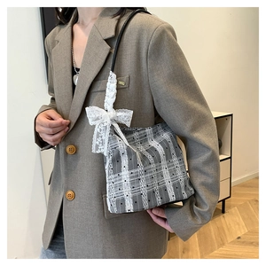 Detail of grey checkered handbag featuring white lace bow and black handle on a model