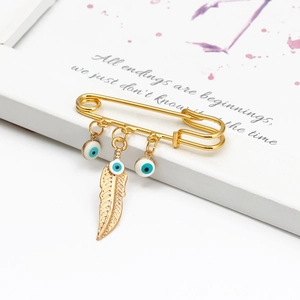 Close-up of golden evil eye pin with enamel beads and textured feather charm detail