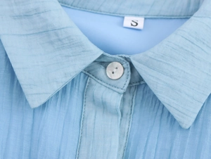 Close-up of light blue sleeveless shirt dress collar with button and pleated texture