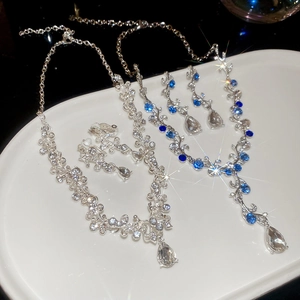 Detail of silver leaf necklace and earrings set with blue gems and rhinestones on a white tray