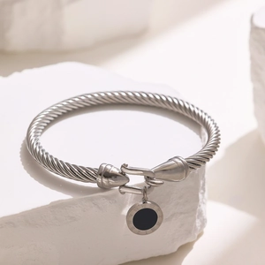 Detail of silver twisted cable bracelet featuring a black Roman numeral pendant charm