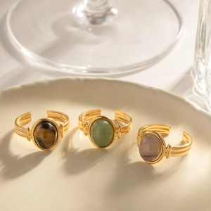Three vintage gold-plated rings with natural semi-precious oval stones on a white tray
