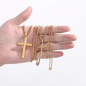 Vue détaillée de deux pendentifs croix en acier doré avec chaînes à mailles carrées