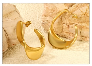 Detailed macro view of gold-plated twisted C-shape earrings on pink stone props