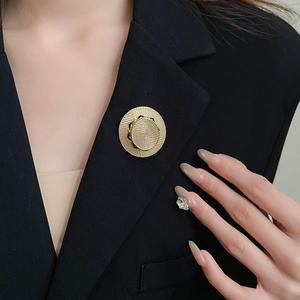 Minimalistische goldene Strohhut-Brosche mit Spiralstruktur auf schwarzem Blazer
