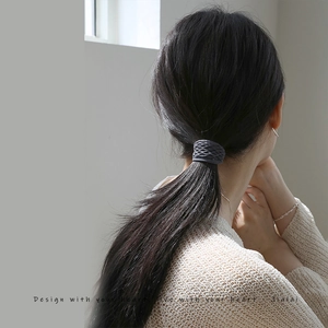 Detail of a gray woven hair tie shown on a ponytail with a stylish and elegant design