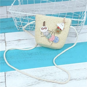 Detailed view of child's straw crossbody bag with colorful caterpillar and flower charms