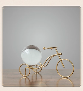 Detail of a gold metal tricycle sculpture holding a clear crystal ball on a wood surface