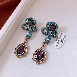 Macro detail of vintage gold snake drop earrings with purple crystals and waterdrop gems