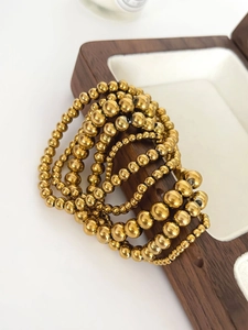 Dettaglio di bracciali con perline placcate oro 18K in varie misure su scatola in legno