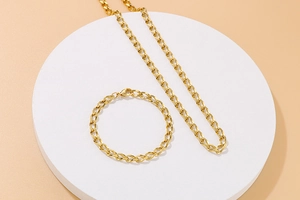 Minimalistisches goldenes Edelstahl-Set aus Halskette und Armband auf einem runden Ständer