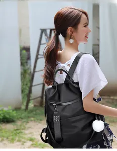 Detail of black nylon backpack with decorative metal rivets and a white pompom charm
