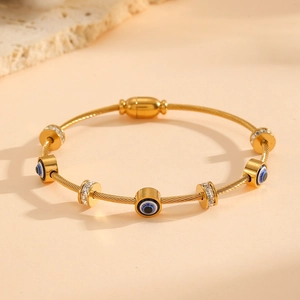 Détail du bracelet tressé doré orné de charms œil bleu et de cristaux étincelants