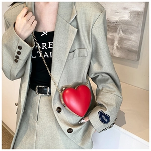 Detail of red heart-shaped leather crossbody bag with gold chain and metal trim