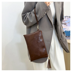 Close-up of brown patchwork clutch bag with stylish fringe tassel and hand strap