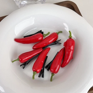 Close-up of red chili hair clips with green stems in a white ceramic dish