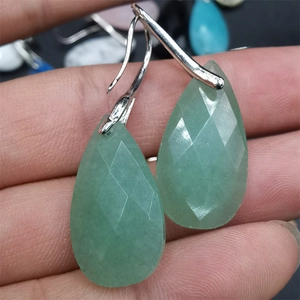 Detailed view of green teardrop-shaped gemstone earrings with silver hooks held by hand
