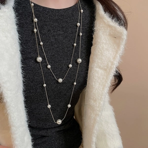 Detailed close-up of double-layer pearl necklace on a grey sweater with golden accents