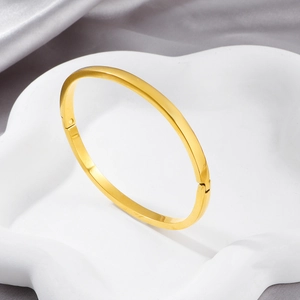 Minimalist gold-plated stainless steel hinged bangle on a white decorative stand