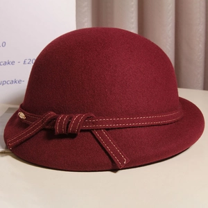 Close-up of vintage burgundy wool cloche hat with stitched ribbon and gold metal accent