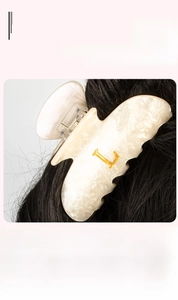 Détail de la pince à cheveux en acrylique marbré crème avec lettre L en métal doré