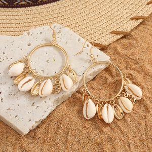 Golden shell hoop earrings on stone background with beach vacation style accessories
