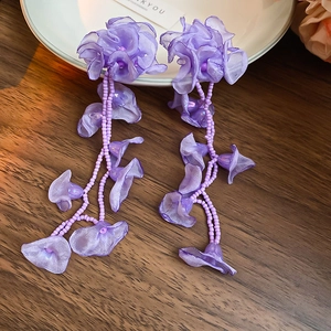 Detailed macro of purple chiffon flower earrings with beaded tassels on wooden table