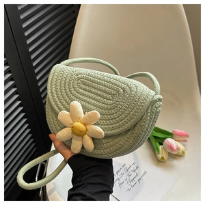 Close-up of light green woven saddle bag featuring a 3D white daisy floral accent