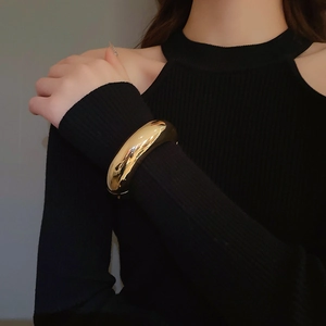 Close-up of polished gold chunky bangle on a model sleeve highlighting minimalist luster