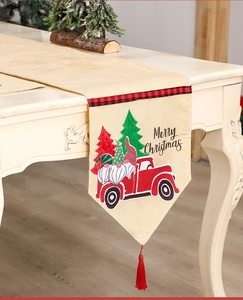 Detail of Christmas table runner with red truck, gnomes, and festive tassels on linen fabric