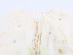 Détails de broderie florale sur blouse crème avec col à cordon et boutons élégants