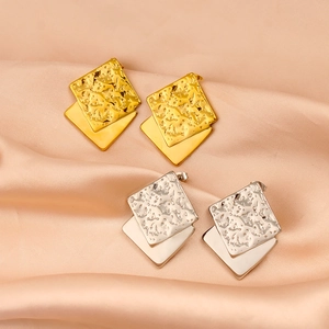Macro shot of double-layered square earrings with textured lava pattern on silk surface