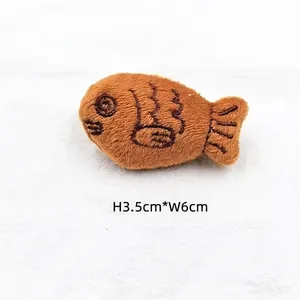 Close-up of plush fish-shaped charm with dimensions 3.5cm by 6cm on white fabric