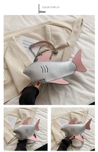 Detail of silver shark-shaped crossbody bag with pink accents and metal chain strap