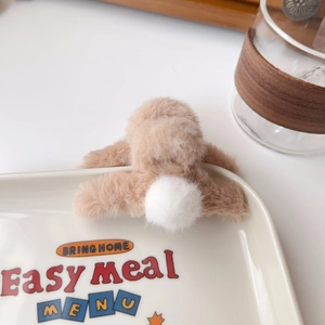 Detail of plush faux fur hair claw clip with white pom-pom on a ceramic plate