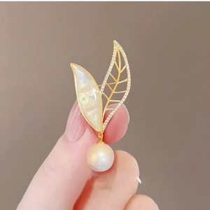 18K gold-plated leaf brooch with white pearls and mother of pearl on a warm background